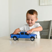 Child playing with a blue toy truck on a light surface.