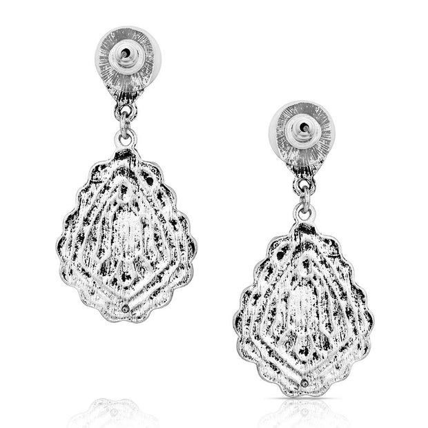 Pair of earrings with turquoise stones and intricate silver designs on a white background