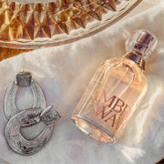 Perfume bottle with Amber Waves branding next to silver horseshoe earrings on a textured surface.