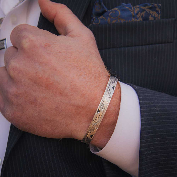 Close-up of a person wearing a gold bracelet with a suit and pocket square in the background