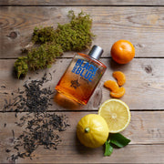 Perfume bottle labeled 'Black and Blue' with lemons, oranges, and tea leaves on a wooden surface