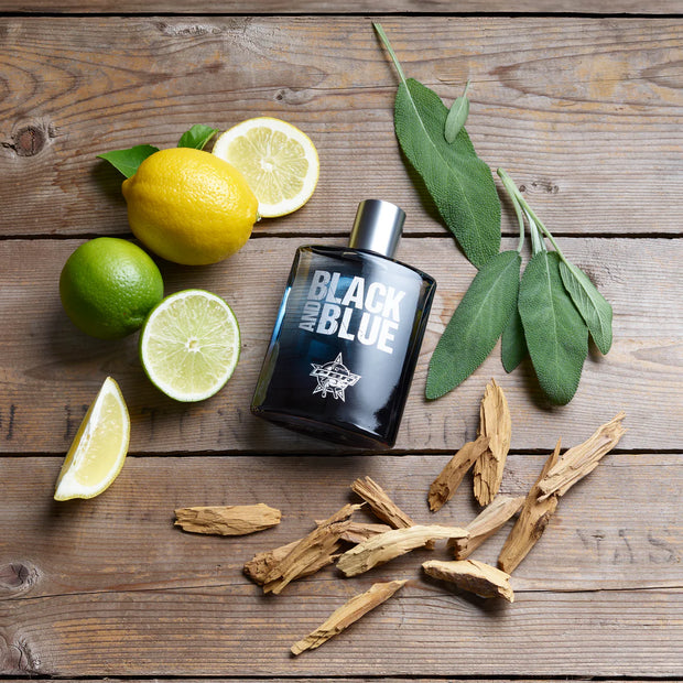 Black and Blue perfume bottle on a wooden surface with lemons, limes, and herbs.