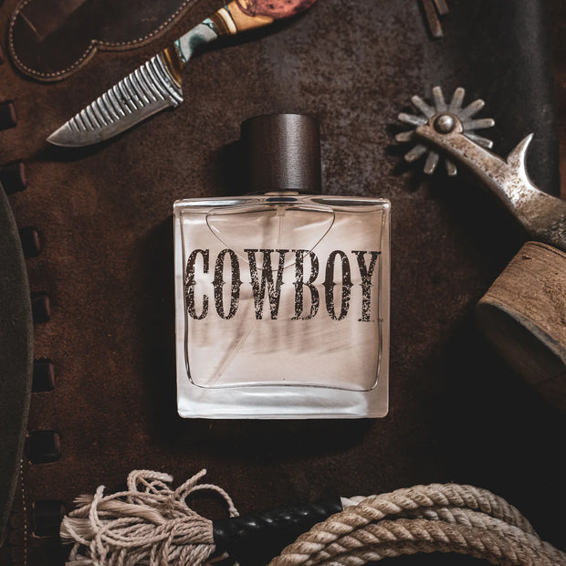 Perfume bottle labeled 'Cowboy' surrounded by cowboy-themed items on a brown background