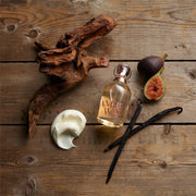 Amber Waves perfume bottle with vanilla beans, figs, and cream on a wooden surface