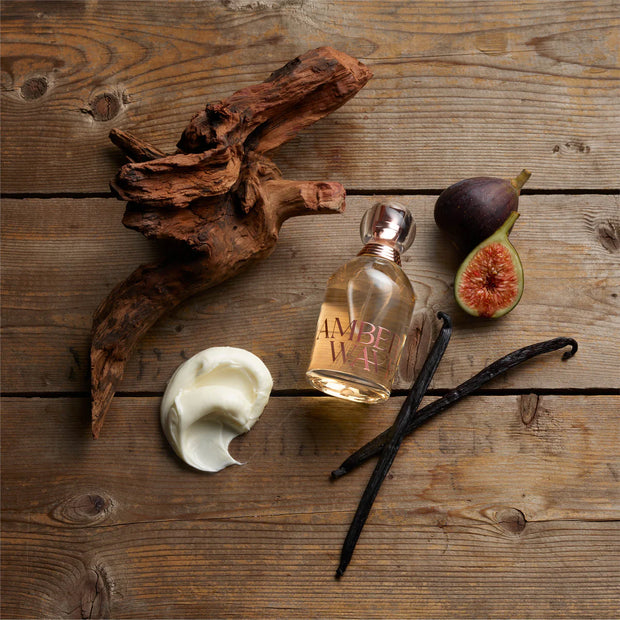 Amber Waves perfume bottle with vanilla beans, figs, and cream on a wooden surface