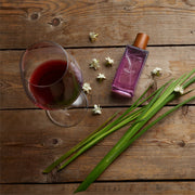 Glass of red wine, purple bottle, and green leaves on a wooden surface