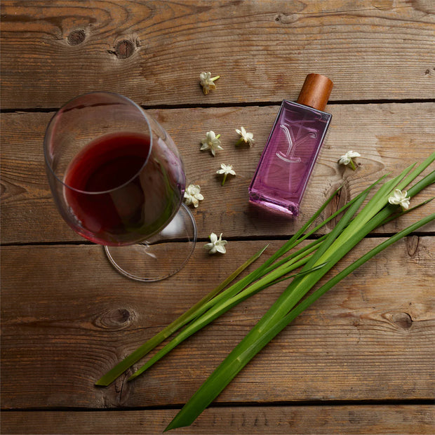 Glass of red wine, purple bottle, and green leaves on a wooden surface