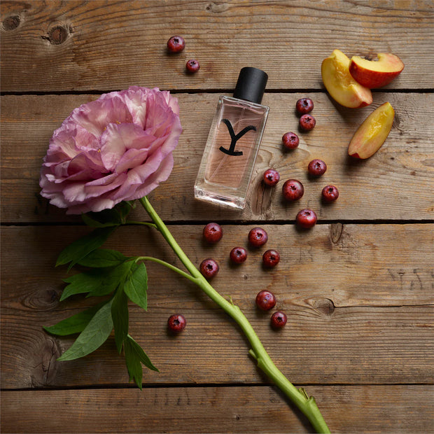 Perfume bottle with a pink flower and fruits on a wooden surface