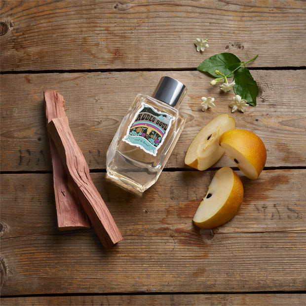Perfume bottle with cinnamon stick and apples on a wooden surface