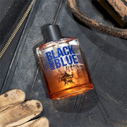 Perfume bottle labeled 'Black and Blue Flame' on a textured surface with gloves and leather goods.