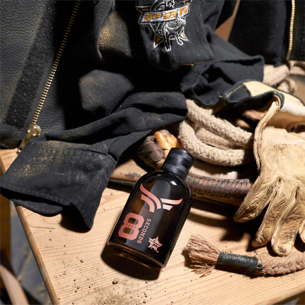 Bottle of 8 Seconds product on a wooden surface with gloves and clothing in the background