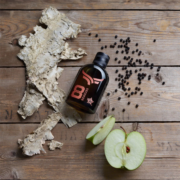 Bottle of B3 Secret on a wooden surface with black peppercorns and a halved green apple.