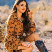 Woman in a patterned shirt sitting outdoors with a blurred natural background