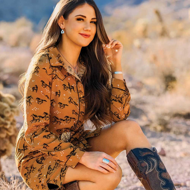 Woman in a patterned shirt sitting outdoors with a blurred natural background
