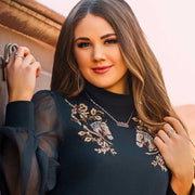 Woman wearing a dark blue dress with floral embroidery, standing against a neutral background.