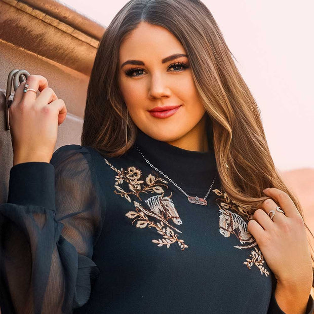 Woman wearing a dark blue dress with floral embroidery, standing against a neutral background.