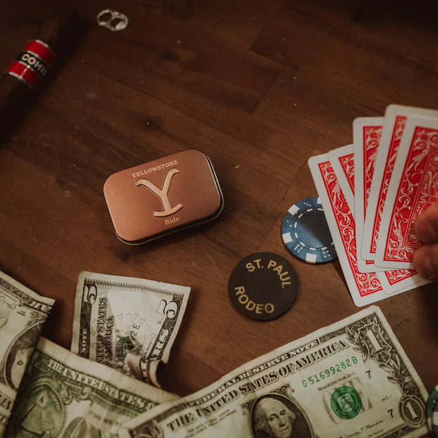 Casino table with money, cards, and a Yuma Rodeo tin on a wooden surface.
