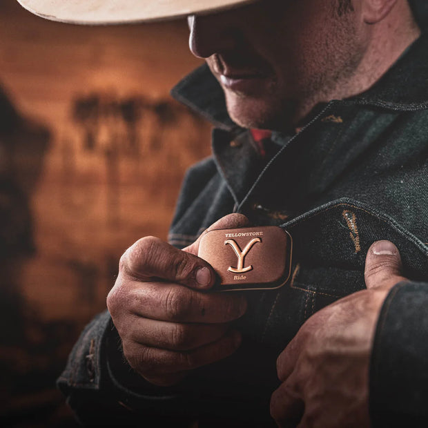 Man holding a leather key fob with 'Yellowstone' branding against a blurred background