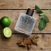 Cowboy Gunslinger perfume bottle on a wooden surface with limes and tobacco leaves.