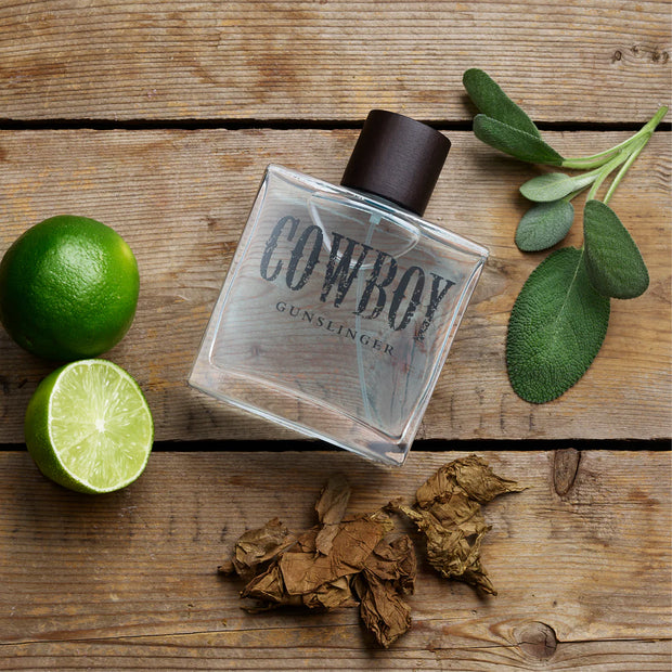 Cowboy Gunslinger perfume bottle on a wooden surface with limes and tobacco leaves.